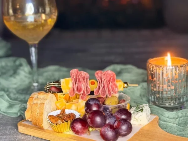 A charcuterie board with meats, cheeses, grapes, and a glass of wine.