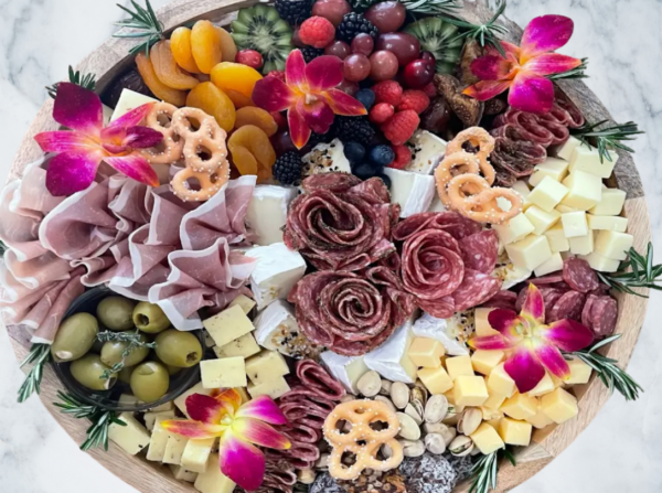 Elegant charcuterie board with meats, cheeses, fruits, and flowers.
