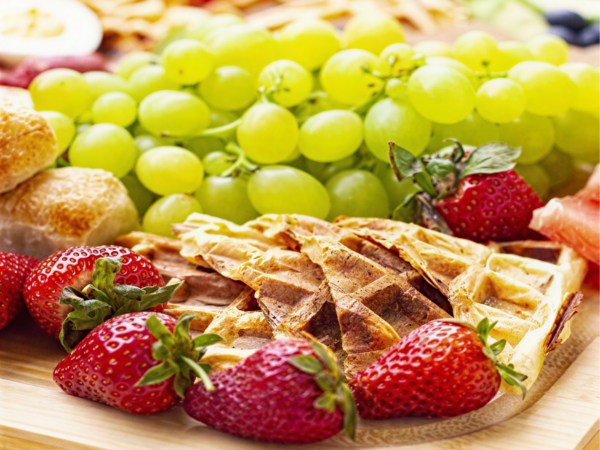 Waffles with strawberries and grapes on a plate.