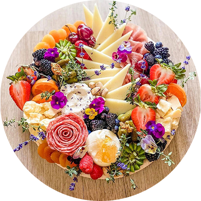 A colorful cheese and charcuterie board with fruits and edible flowers.